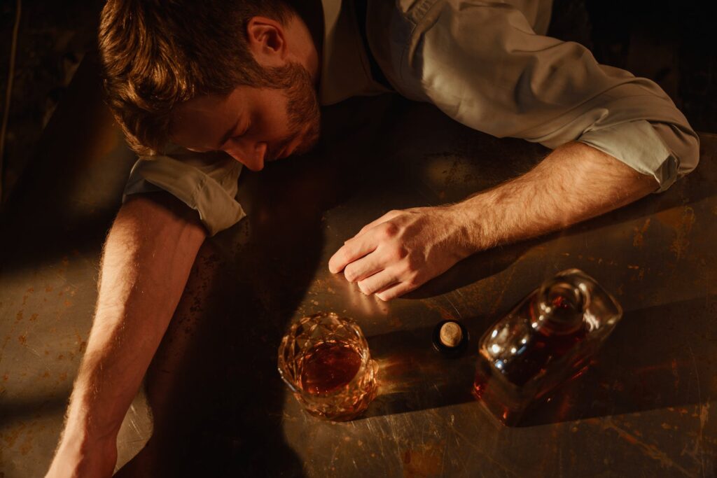 a man sleeps on a table with a bottle of whiskey