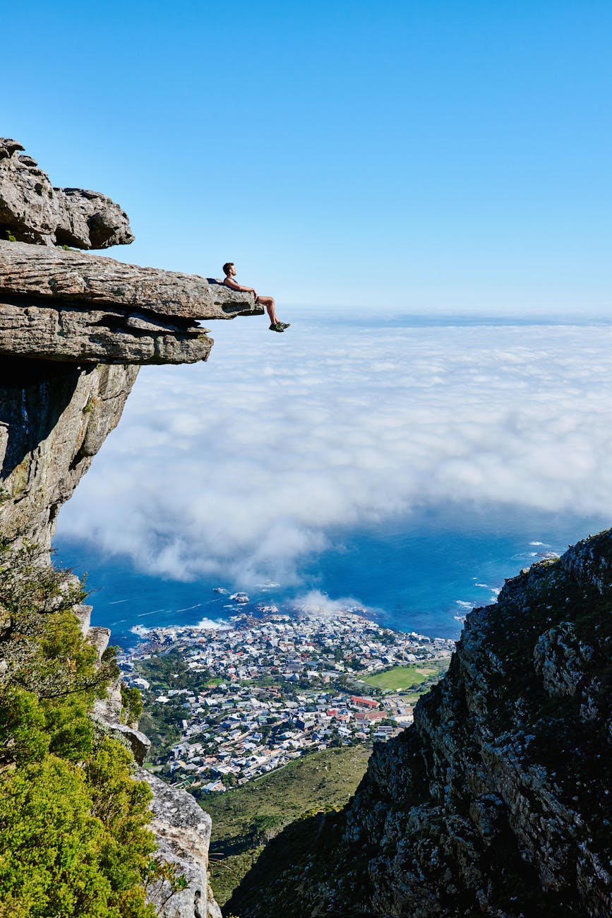 person sitting on mountain cliff: The poem opens with the personification of nature, framing climate change as a message—an alarm that humanity must heed. This sets the tone: the Earth is in crisis, and it is calling out for rescue.