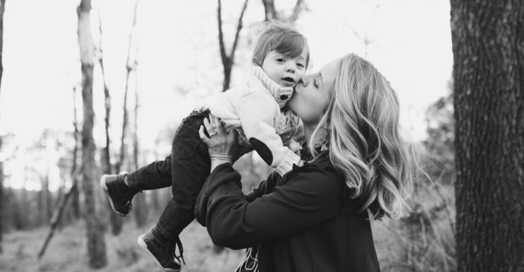 grayscale photo of woman kissing toddler on cheek. This poem, "Magnanimous Mother," beautifully narrates the life of a child who loses his mother at a young age, detailing his upbringing by relatives and his enduring, unseen connection to his mother throughout his journey to adulthood, culminating in the hope of reunion in Heaven.